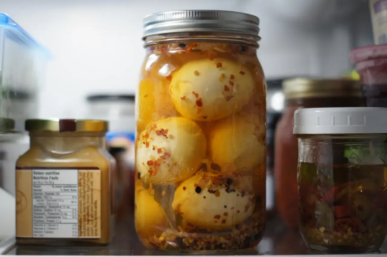 Un bocal rempli d'oeufs au vinaigre, épicés et conservés dans un liquide ambré, se trouve au premier plan.
