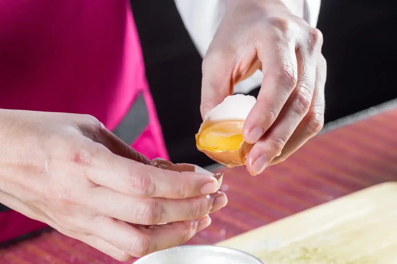 Mains séparant délicatement le jaune d'œuf blanc de sa coquille.